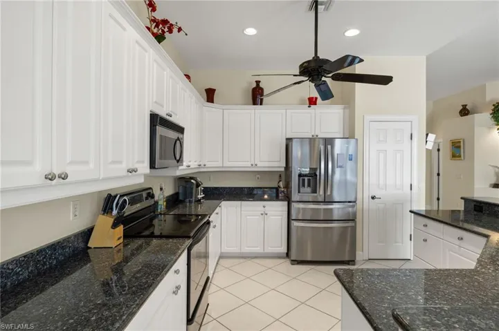 Kitchen with white cabinets, stainless steel appliances, light tile patterned flooring, visible vents, and a ceiling fan