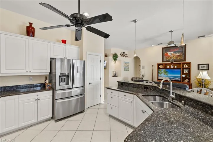 Kitchen featuring a ceiling fan, a sink, light tile patterned flooring, stainless steel refrigerator with ice dispenser, and white cabinetry