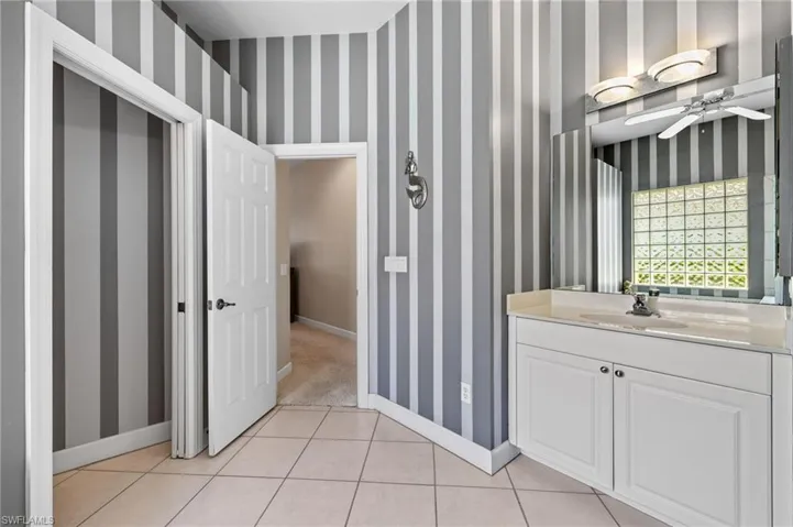 Bathroom with wallpapered walls, tile patterned flooring, baseboards, and ceiling fan