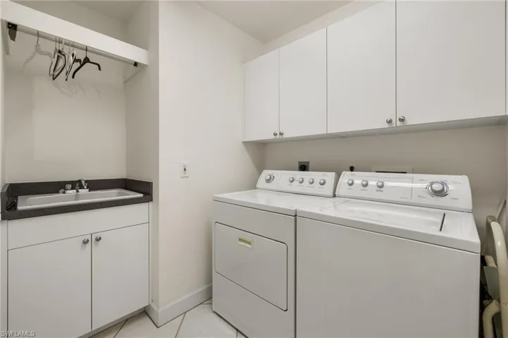 Washroom with a sink, light tile patterned floors, cabinet space, baseboards, and independent washer and dryer
