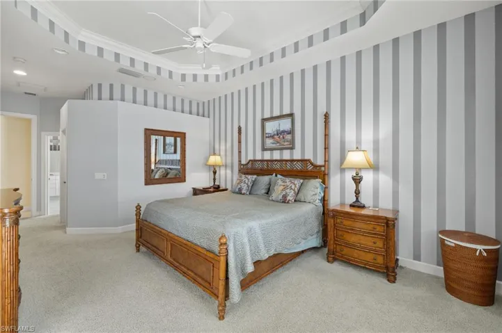 Bedroom with ceiling fan, light colored carpet, baseboards, ornamental molding, and visible vents