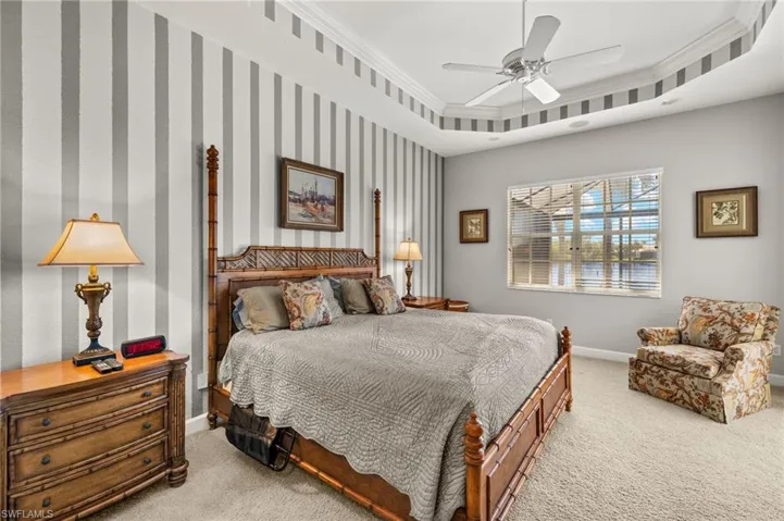 Carpeted bedroom with ceiling fan, baseboards, crown molding, and a tray ceiling