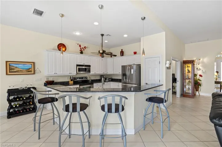 Kitchen with stainless steel appliances, a breakfast bar, visible vents, light tile patterned flooring, and white cabinetry