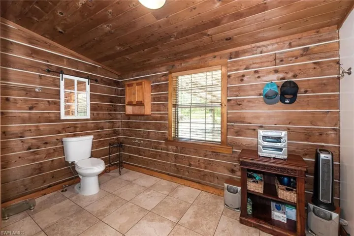 Bathroom featuring vaulted ceiling, wood walls, wooden ceiling, toilet, and tile patterned floors