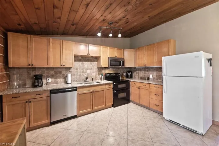 Kitchen with a sink, light stone counters, backsplash, stainless steel appliances, and light tile patterned floors
