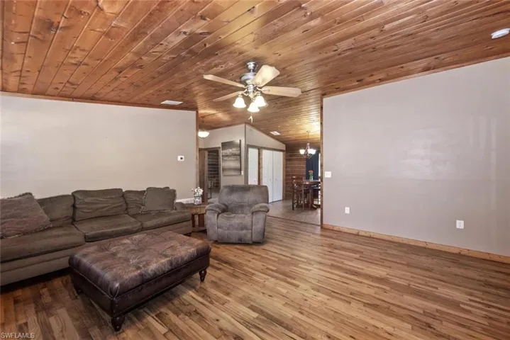 Living area featuring ceiling fan with notable chandelier, wood finished floors, baseboards, wood ceiling, and vaulted ceiling