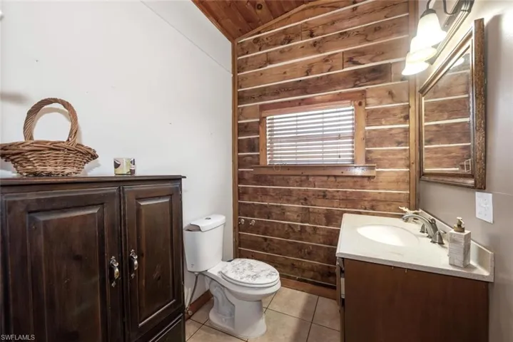 Bathroom with tile patterned floors, toilet, wooden walls, vanity, and vaulted ceiling