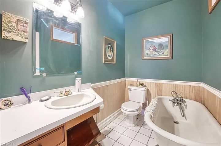 Bathroom with tile patterned flooring, a wainscoted wall, toilet, a freestanding tub, and vanity