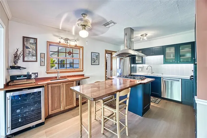 Kitchen featuring visible vents, beverage cooler, island exhaust hood, a sink, and stainless steel appliances