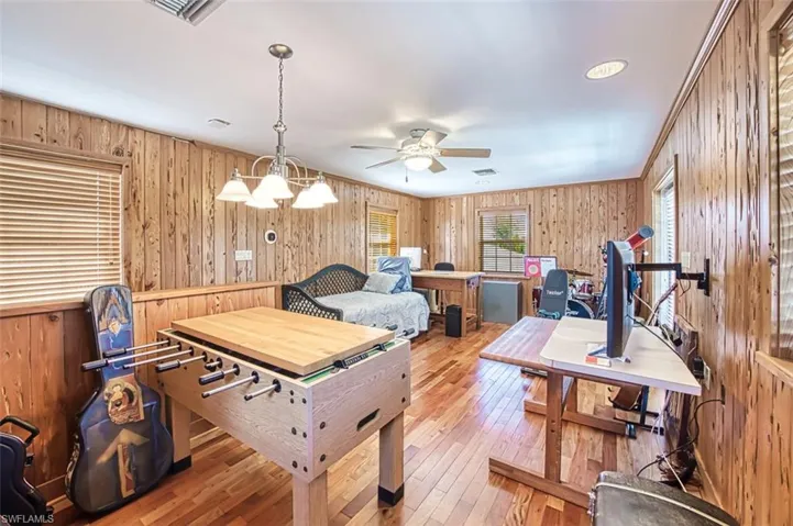 Rec room featuring hardwood / wood-style flooring, wooden walls, ceiling fan with notable chandelier, and visible vents