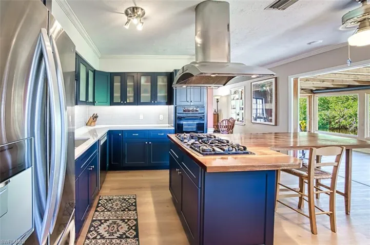Kitchen with island range hood, blue cabinetry, ornamental molding, stainless steel appliances, and butcher block counters