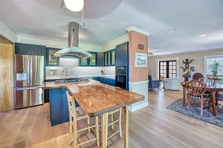 Kitchen with blue cabinetry, island exhaust hood, light wood-style floors, and appliances with stainless steel finishes