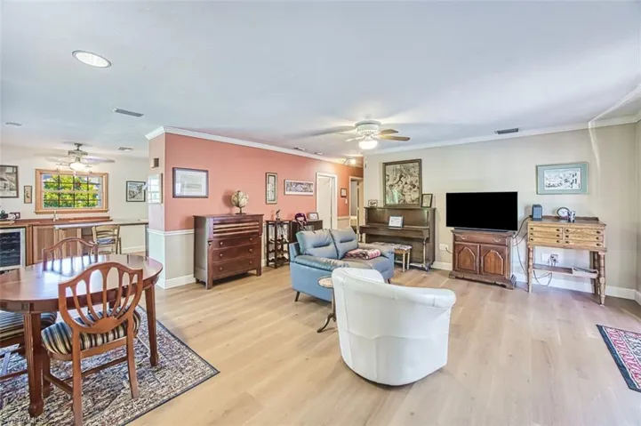 Living room with a ceiling fan, wine cooler, light wood-style floors, and crown molding