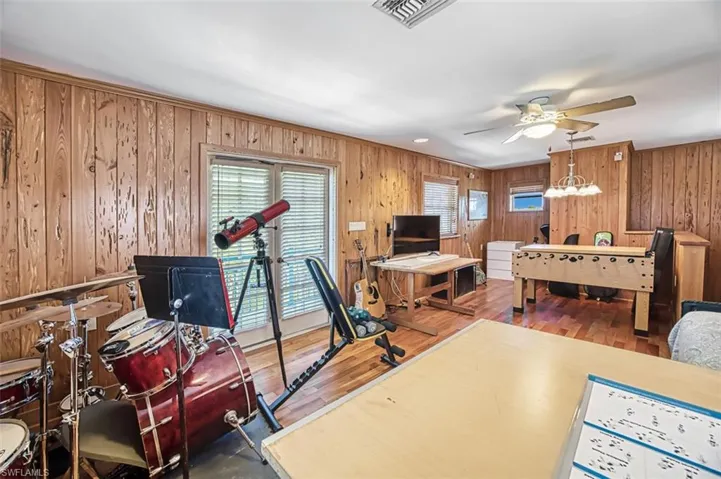 Bedroom with wooden walls, a ceiling fan, wood finished floors, visible vents, and access to outside
