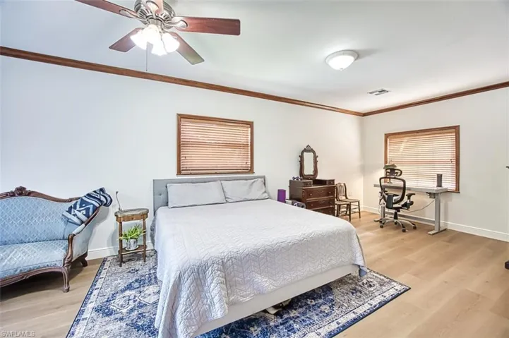 Bedroom with visible vents, baseboards, light wood-style floors, and ornamental molding