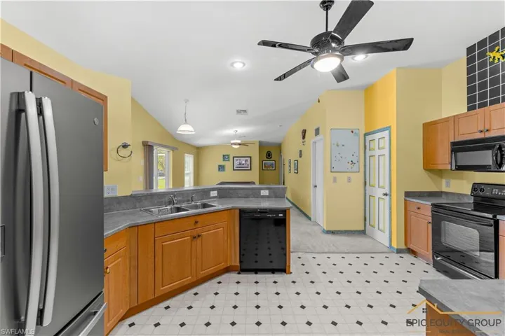 Kitchen with black appliances, ceiling fan, decorative light fixtures, vaulted ceiling, and light floors