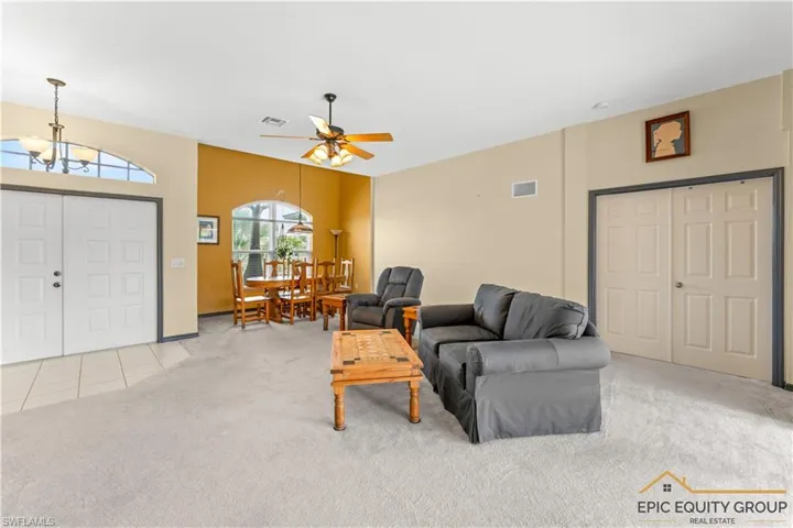 Living area with light carpet, ceiling fan, a chandelier, and light tile patterned floors