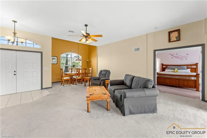 Living area featuring light carpet, a ceiling fan, hanging lights, and light tile patterned flooring
