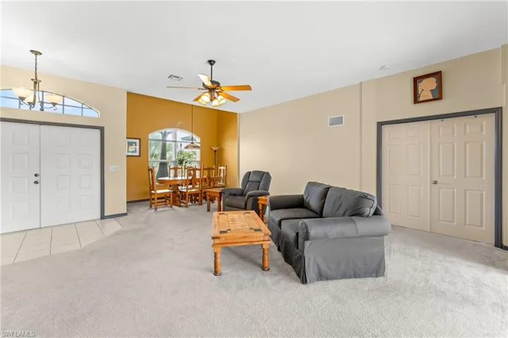 Living area featuring light colored carpet, ceiling fan, a chandelier, and light tile patterned floors
