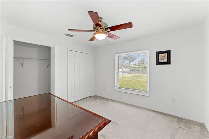Unfurnished bedroom featuring light carpet, a ceiling fan, and two closets