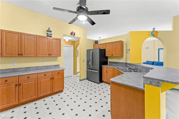 Kitchen with arched walkways, a peninsula, light floors, stainless steel fridge, and wood finish cabinetry