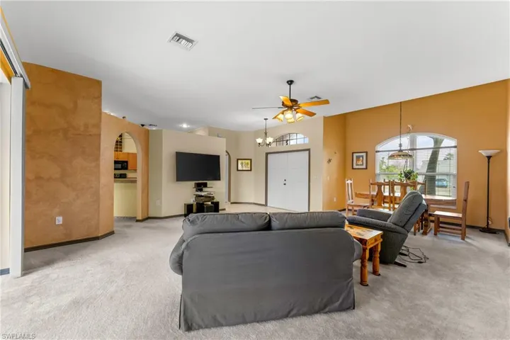 Living area with light carpet, arched walkways, a ceiling fan, and a chandelier
