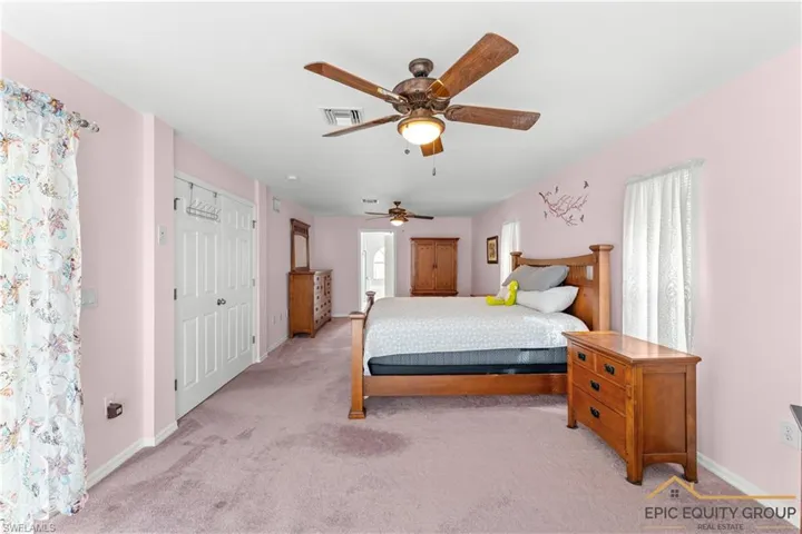 Bedroom featuring a ceiling fan, light colored carpet, a closet, and ensuite bathroom