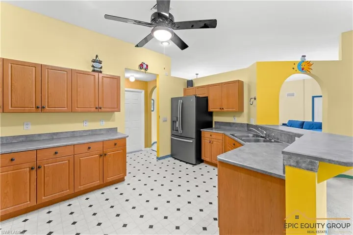 Kitchen featuring arched walkways, a peninsula, light floors, stainless steel fridge, and wood finish cabinetry