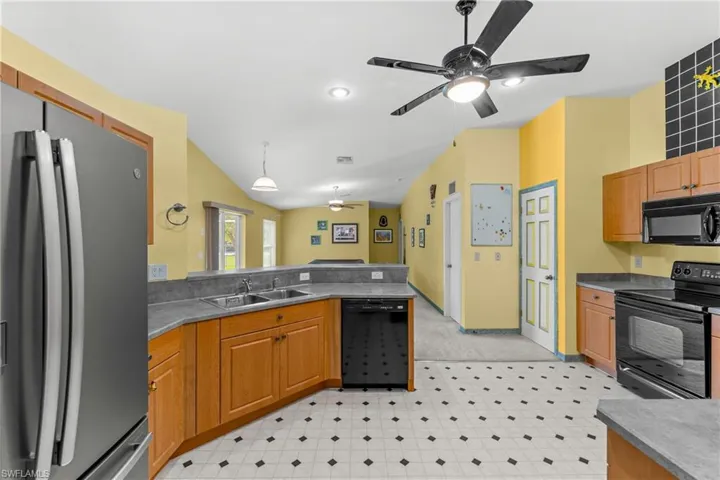 Kitchen with black appliances, a ceiling fan, decorative light fixtures, vaulted ceiling, and light floors