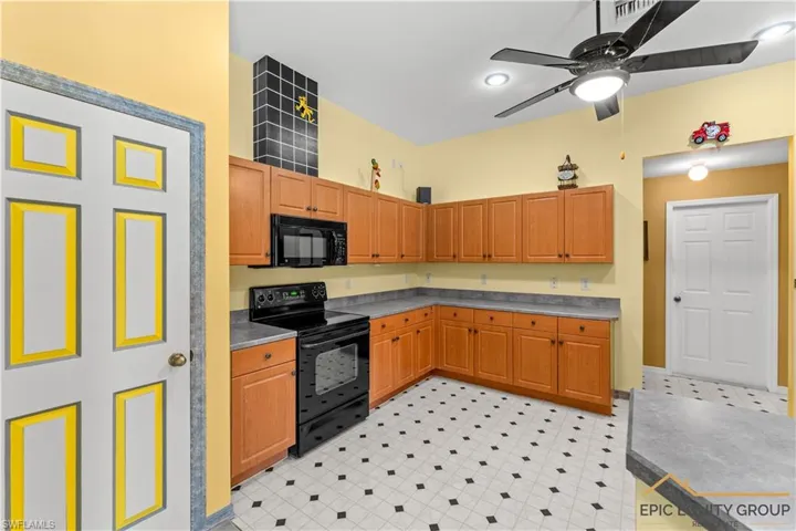 Kitchen with black appliances, ceiling fan, light flooring, and dark countertops