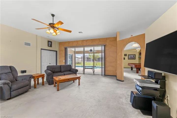 Living room with ceiling fan, light colored carpet, arched walkways, and billiards table