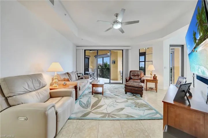 Living room with a raised ceiling, light tile patterned floors, and a ceiling fan