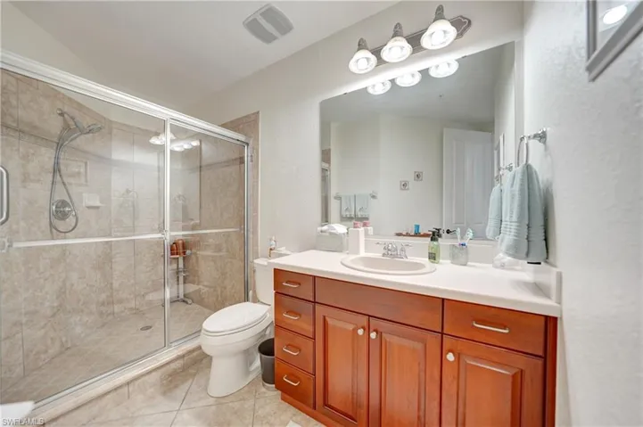 Full bath featuring vanity, a textured wall, light tile patterned floors, and a stall shower