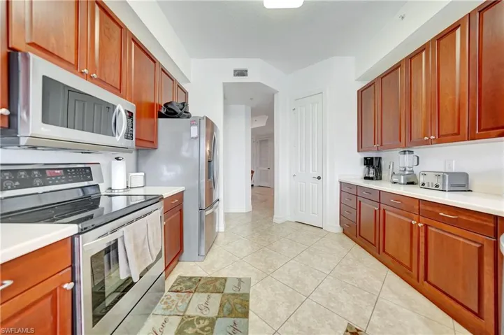 Kitchen featuring stainless steel appliances, light countertops, light tile patterned floors, and brown cabinetry