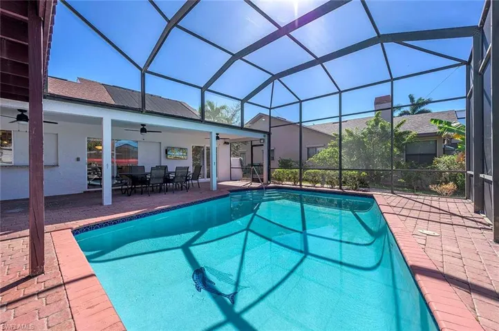 Swimming pool with a ceiling fan, a patio area, outdoor dining space, and glass enclosure