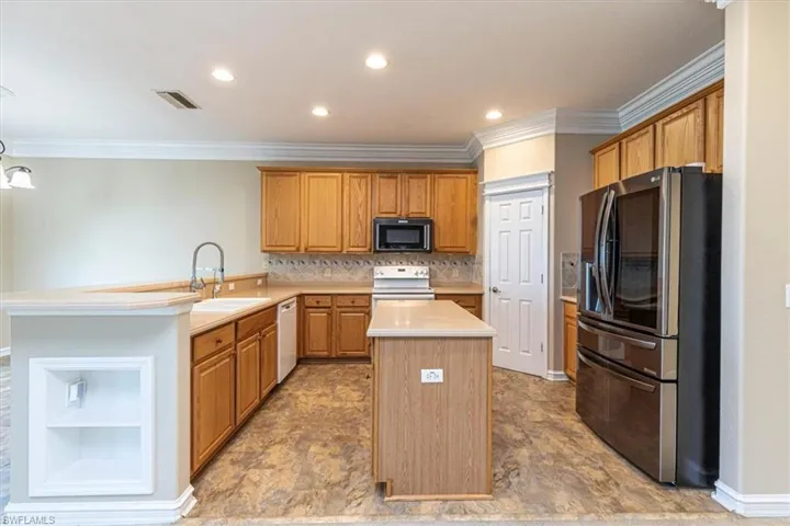 Kitchen featuring white appliances, a peninsula, light countertops, a kitchen island, and ornamental molding