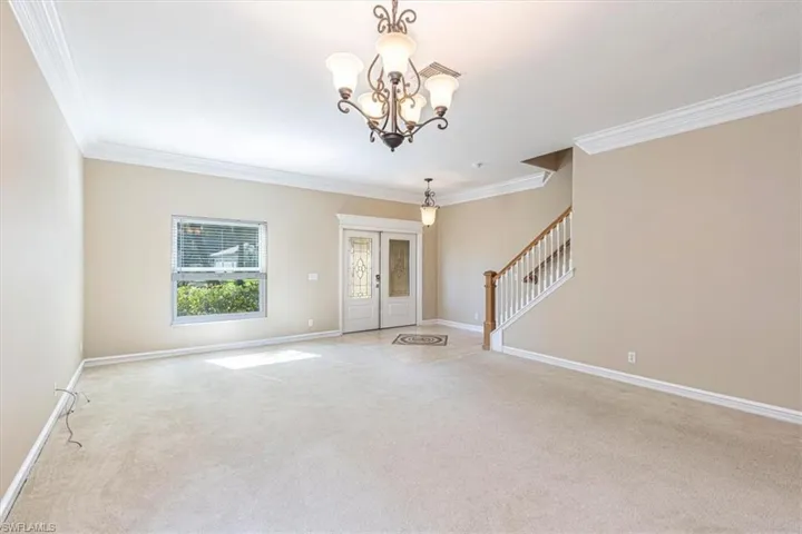 Carpeted foyer entrance with stairway, French doors, chandelier & crown molding.