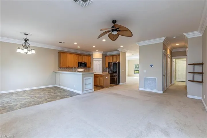 Kitchen featuring open floor plan, light colored carpet, brown cabinets, fridge with ice dispenser & ornamental molding.
