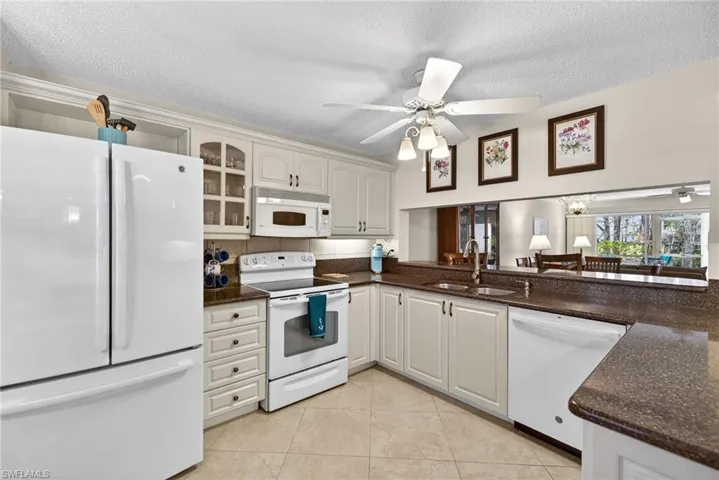 Kitchen featuring white appliances, a textured ceiling, dark stone counters, a ceiling fan, and light tile patterned floors