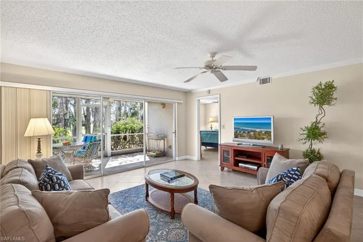 Living room featuring a ceiling fan, a textured ceiling, tile patterned floors, and crown molding
