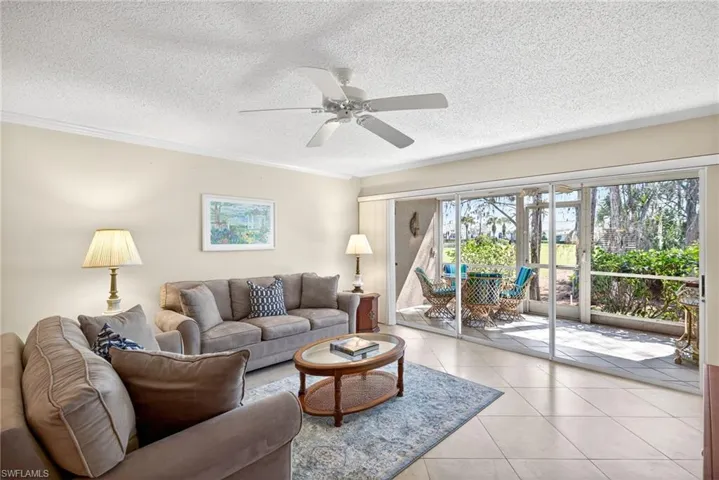 Living room with a textured ceiling, tile patterned floors, ceiling fan, and crown molding