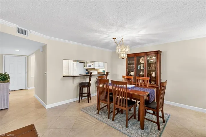 Dining area featuring crown molding, a chandelier, light tile patterned floors, and a textured ceiling
