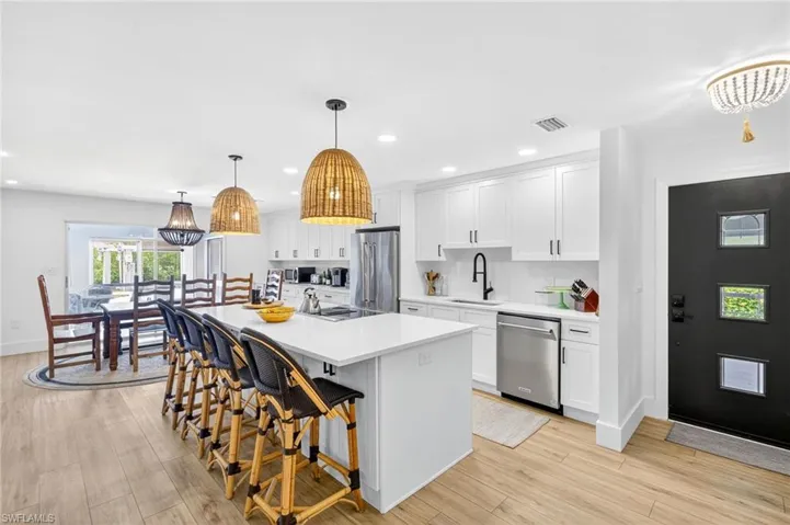 Kitchen featuring a breakfast bar area, white cabinetry, a center island with sink, hanging light fixtures, and appliances with stainless steel finishes