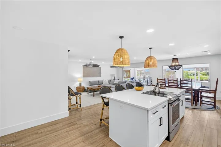 Kitchen featuring electric range, a kitchen island with sink, open floor plan, pendant lighting, and healthy amount of natural light