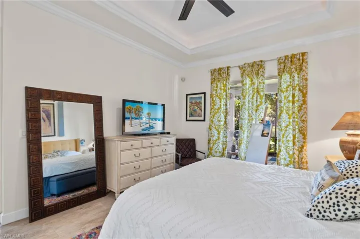 Bedroom featuring light wood-type flooring, ceiling fan, a raised ceiling, and ornamental molding. Lake view.