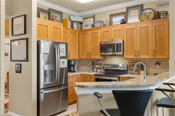 Kitchen featuring crown molding, tasteful backsplash, kitchen peninsula, stainless steel appliances, and a kitchen breakfast bar.