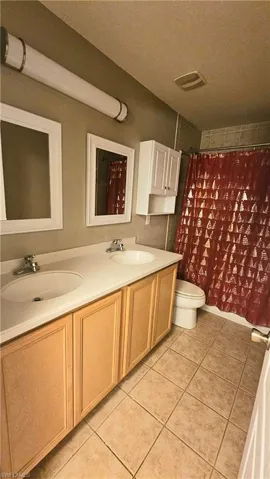 Bathroom featuring a shower with shower curtain, vanity, a textured ceiling, tile patterned flooring, and toilet