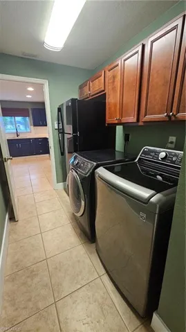 Washroom featuring washer and dryer, light tile patterned flooring, cabinets, and a textured ceiling