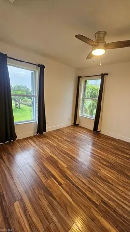 Empty room with dark hardwood / wood-style flooring, a wealth of natural light, and ceiling fan
