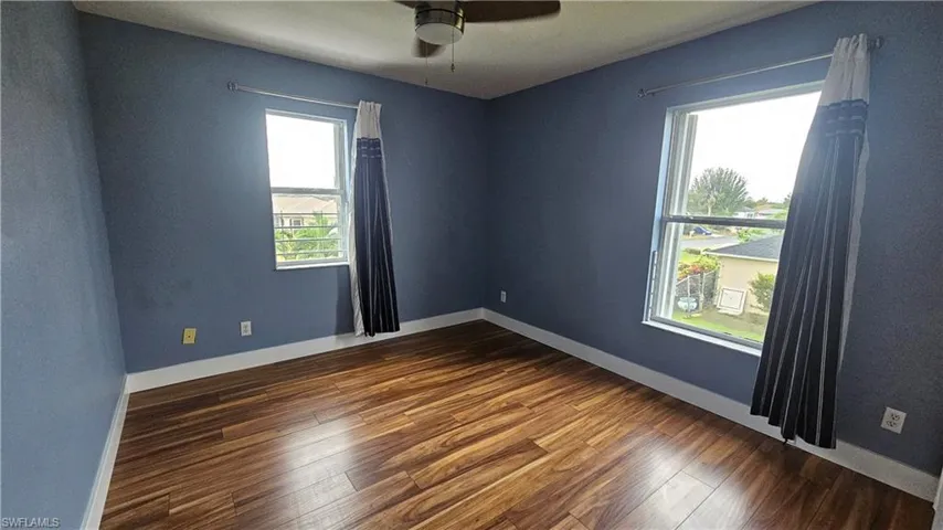 Spare room featuring ceiling fan, a healthy amount of sunlight, and dark wood-type flooring